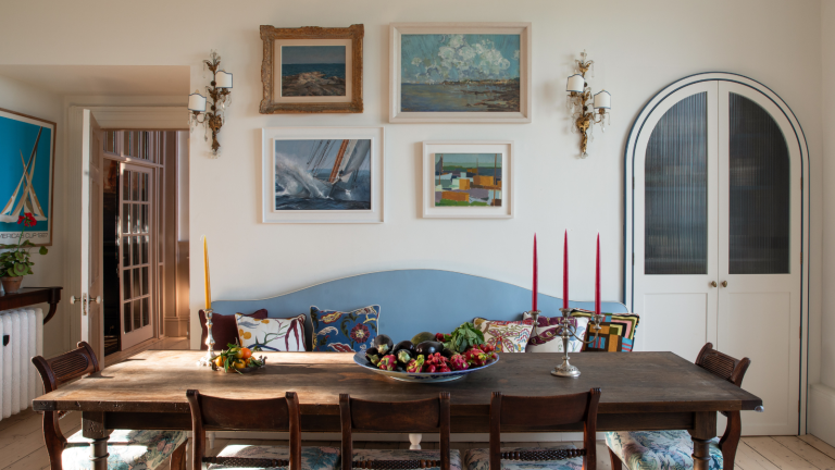 6 choses que les designers d’intérieur font toujours à Round Top Texas pour obtenir les meilleures trouvailles vintage Dining room with a long mahogany table and chairs, a blue banquette, a gallery wall of vintage pictures, and antique candlesticks and sconces