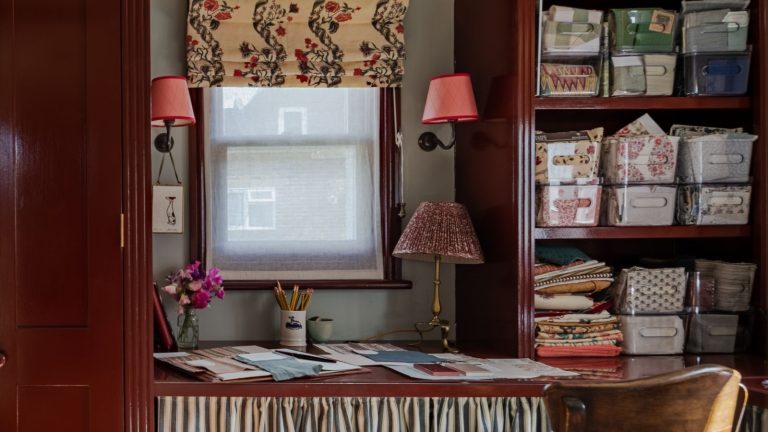 Je pensais que les bacs en plastique étaient une horreur, mais les conseils de style haut de gamme de ce créateur m’ont fait changer d’avis – vous ne sauriez jamais qu’il s’agissait d’achats de base sur Amazon Small home office with red painted built-in cupboards, built-in desk with skirted fabric, and an open cupboard with plastic containers holding stationary