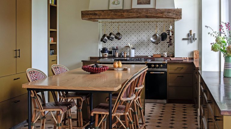 Les comptoirs en cuivre sont devenus la tendance improbable qui a propulsé ce château français « sans prétention » dans le 21e siècle a french farmhouse style kitchen in a Chateau near Paris with a large kitchen table and bistro chairs, traditional stone floor, green ochre cabinetry, black range cooker and large cooker hood