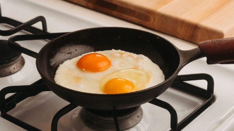Cette erreur d’anneau thermique ruine votre saisie en fonte – Comment arrêter de coller et de brûler en quelques secondes Field Company Cast Iron Skillet with two frying eggs inside on a gas stove.