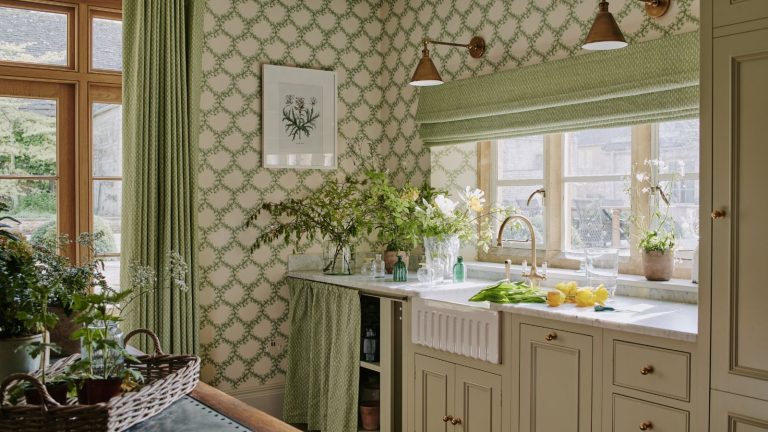 L’édition très britannique : comment une réinitialisation réfléchie du nettoyage de printemps peut rétablir l’ordre, éliminer l’encombrement et apporter le calme à votre maison spring decorated beige shaker kitchen with a fluted sink and green decor including floral foliage wallpaper with an under sink cabinet skirt with brass wall lights