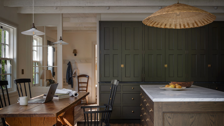 La cuisine industrielle chaleureuse – 24 pièces pour que même l’espace le plus utilitaire se sente comme le cœur de la maison a rustic kitchen with a large wooden table and several chairs, a kitchen island with a marble countertop, a wall of cabinets painted in a deep green color, and a large rattan pendant lamp