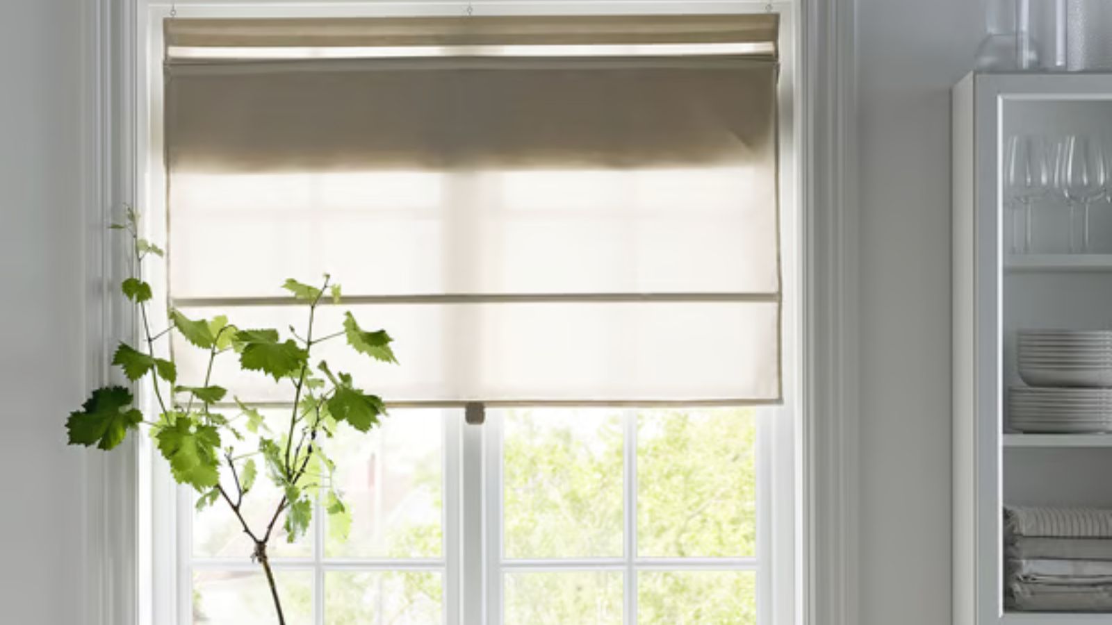 Store en lin neutre sur fenêtre de cuisine avec étagères et vaisselle à droite