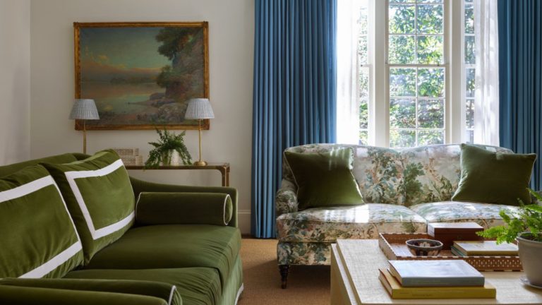 Rencontrez « Serene Earth » : les concepteurs de palettes de salon apaisants (mais controversés) n’en ont jamais assez Living room with blue drapes and large French door, floral sofa with green cushions and a green velvet sofa, wooden coffee table with books and decor and an antique landscape above a console in the corner