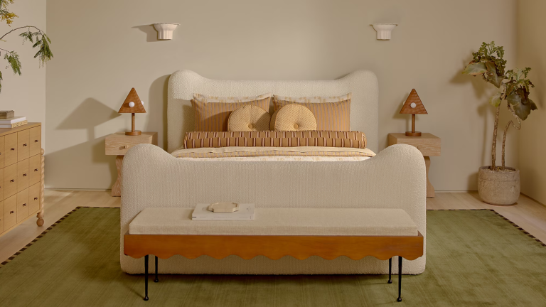 La nouvelle collection inspirée des hôtels Lulu et Georgia de Sarah Sherman Samuel prouve que les intérieurs ludiques peuvent toujours être chics a warm, whimsical bedroom with a green rug, a white upholstered bed, a bench at the foot of the bed, and pillows on the bed