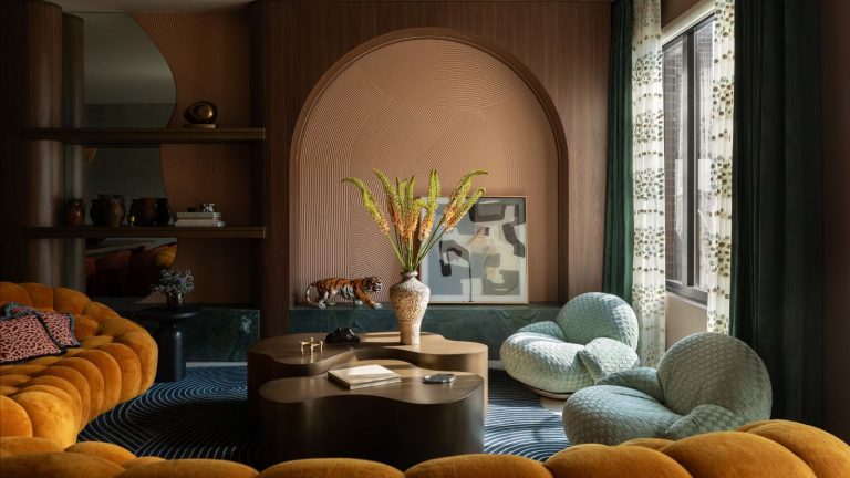 Arrêtez la lutte télévisée « murmurante jusqu’à l’explosion » – Cette barre de son Bose a enfin mis fin à mon réglage constant du volume Abstract and colorful living room with curved coffee table, large potted plant, orange, round, padded sofa, and two soft chairs. A wooden archway and shelves with miscellaneous ornaments are pictured in the background.