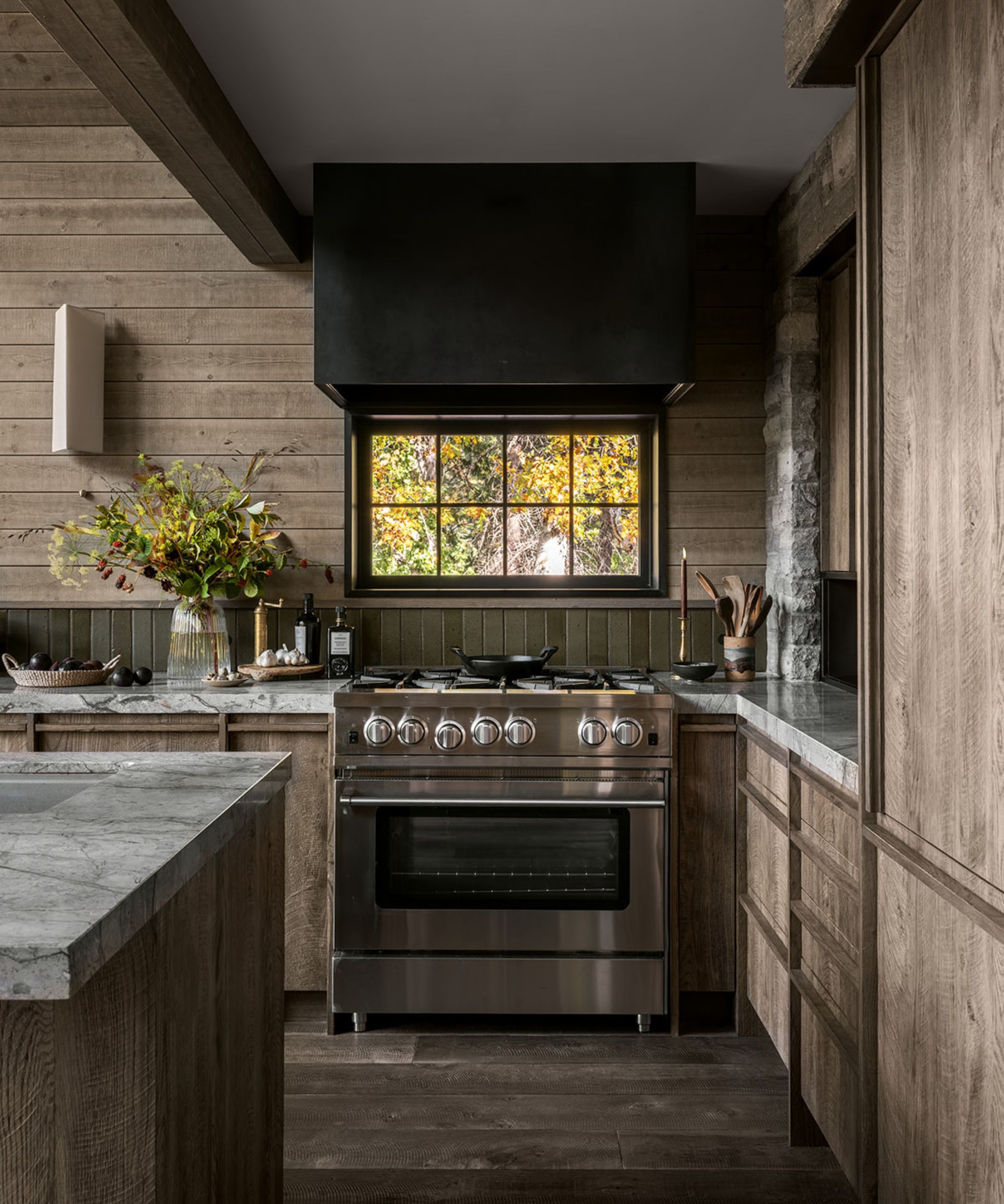 Une cuisine cabine avec des armoires en bois, des comptoirs en marbre et un dosseret en matériaux mixtes avec des carreaux verts et des panneaux de bois