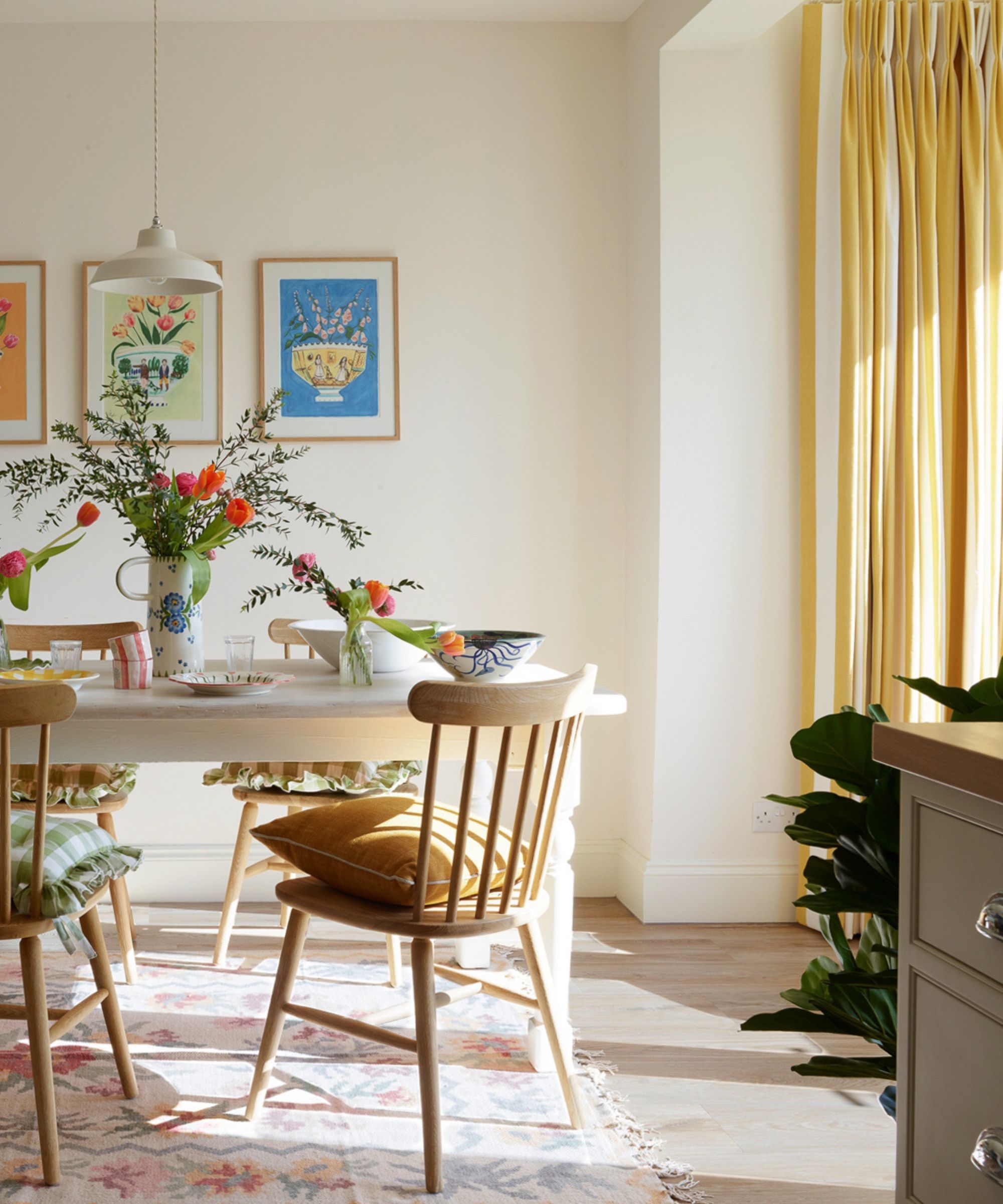 Salle à manger de style scandinave avec murs blancs, table en bois blanc, chaises en bois, rideaux jaunes et tapis fleuri