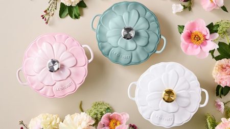 Three pastel, floral-design Le Creuset Dutch Ovens on a off-white bakground, surrounded by pink and white flowers