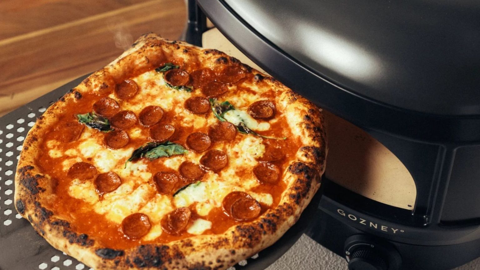 Le nouveau four à pizza compact de Gozney transforme le stress culinaire de Pâques en festins en plein air de qualité restaurant – rapide, facile et qui plaira à tous A cooked pepperoni pizza coming out of a black slimline pizza oven on a perforated pizza slice.