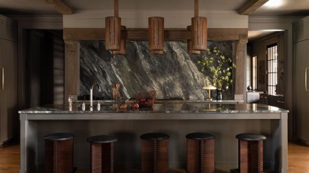 Open-plan farmhouse kitchen with a large marble island, dark marble backsplash, reclaimed wood beams, and vintage wooden stools.