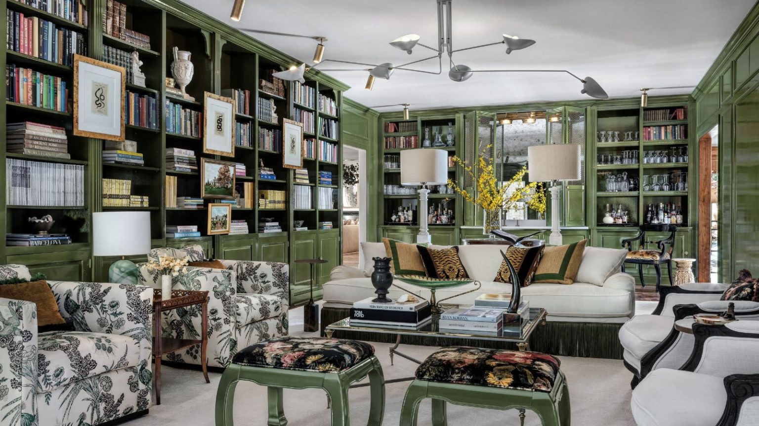 Les architectes d’intérieur partagent l’astuce simple d’une bibliothèque qui donne à votre maison un aspect plus habité – « Elle transforme la bibliothèque en une toile de fond évolutive, presque comme un collage vivant » Living room with green painted bookshelves, cream sofa and armchairs, midcentury pendant light, green stools
