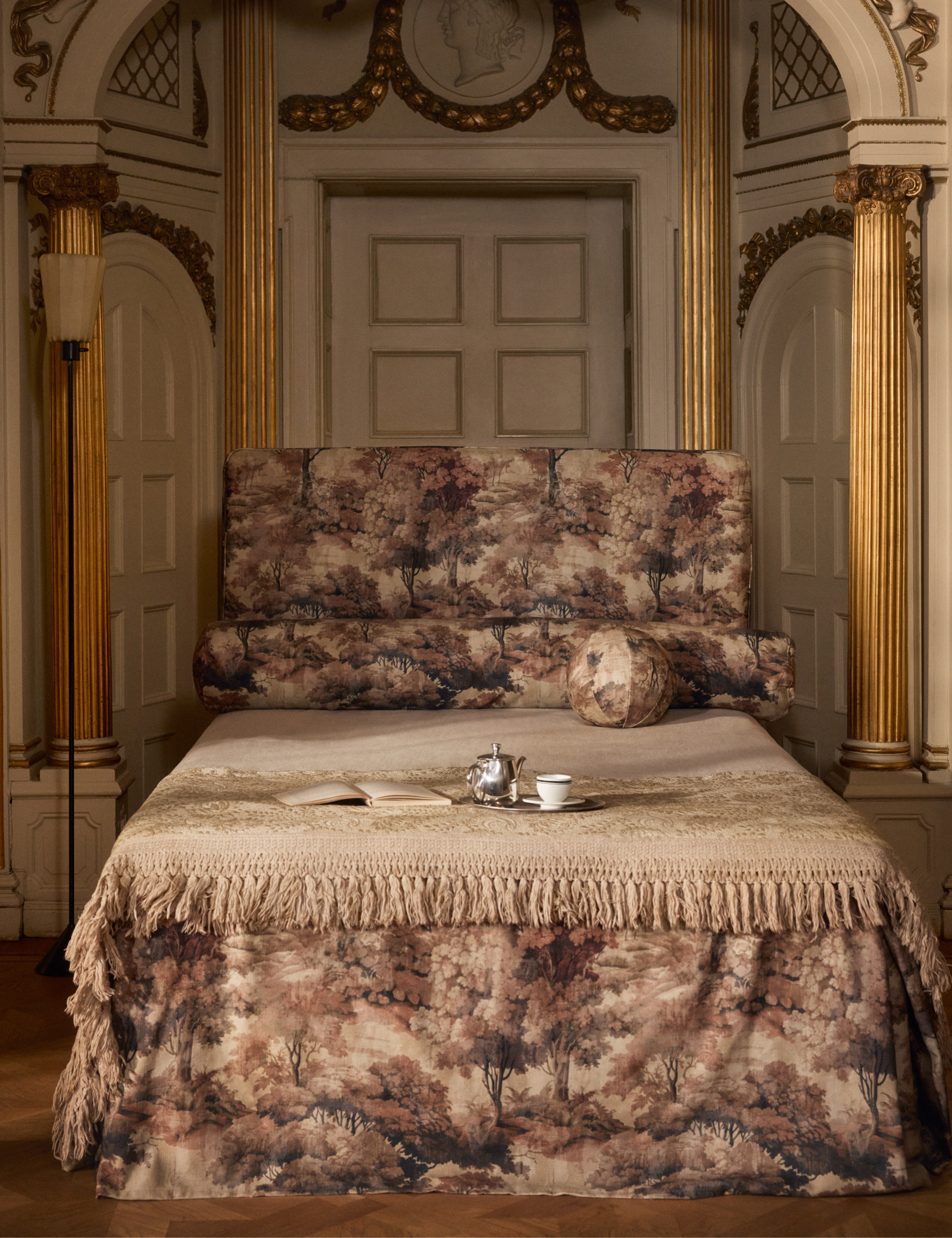 Chambre opulente avec des murs dorés vert et or et un lit recouvert d'une tapisserie, orné d'un livre et d'un service à thé.