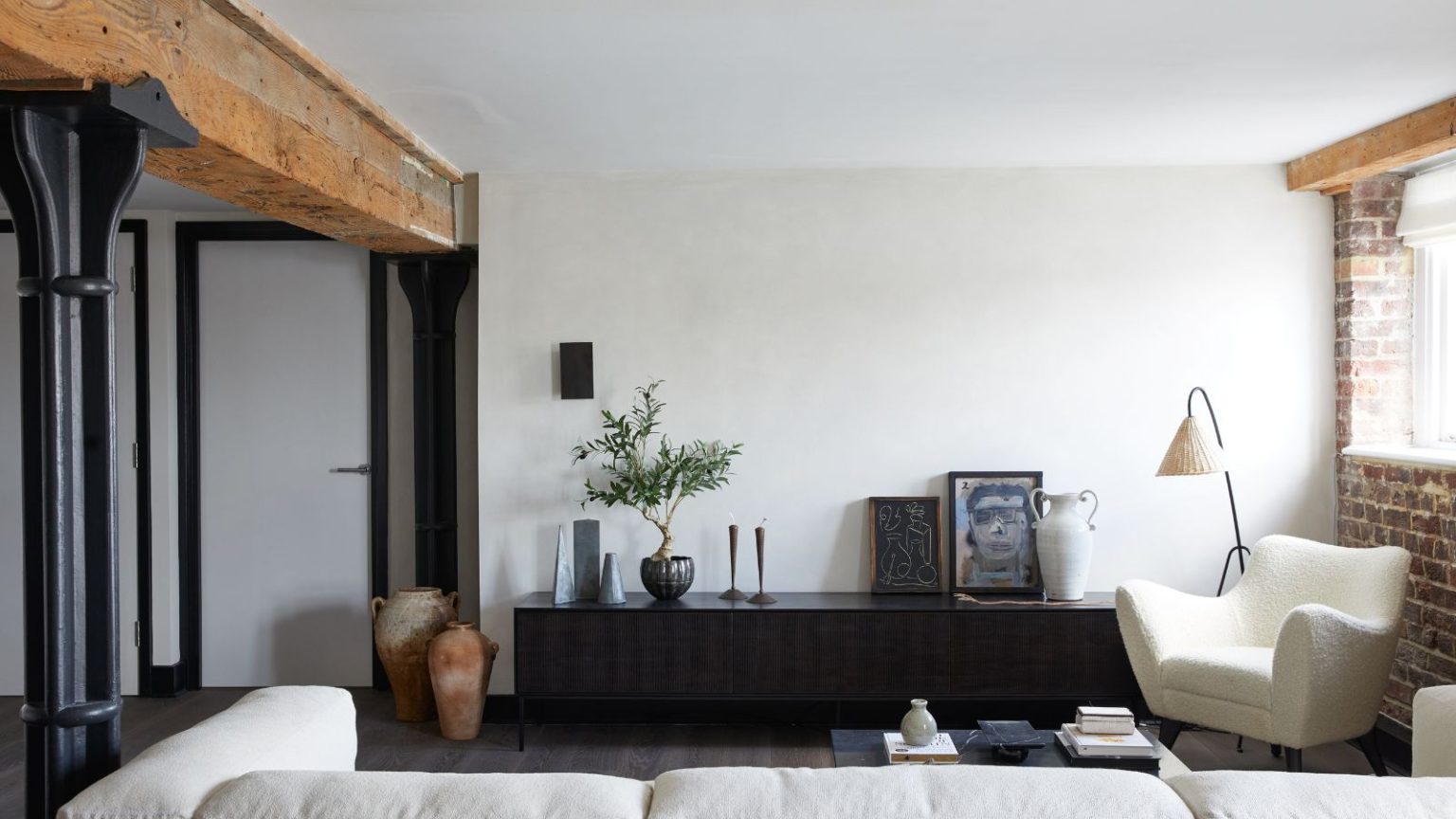 Arrêtez d’accrocher vos œuvres d’art, toutes les maisons les plus chics adoptent cette approche plus décontractée de la décoration avec des imprimés – et vous pouvez passer au zéro dommage en quelques minutes. Industrial loft style living room with exposed beams and brick wall, plaster walls, console table with artwork and potted plant, boucle chair, white sofa and floor lamp