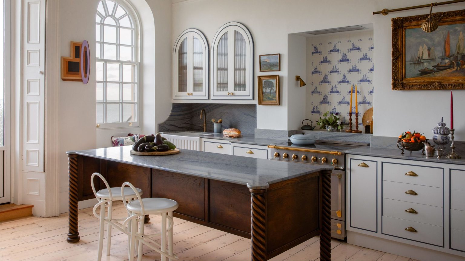 Cette maison de Dublin des années 1790 possède un tunnel caché menant à la plage. À l’intérieur, les intérieurs sont tout aussi oniriques a white coastal kitchenin dublin with a dark wooden vintage style island and arched cabinetry