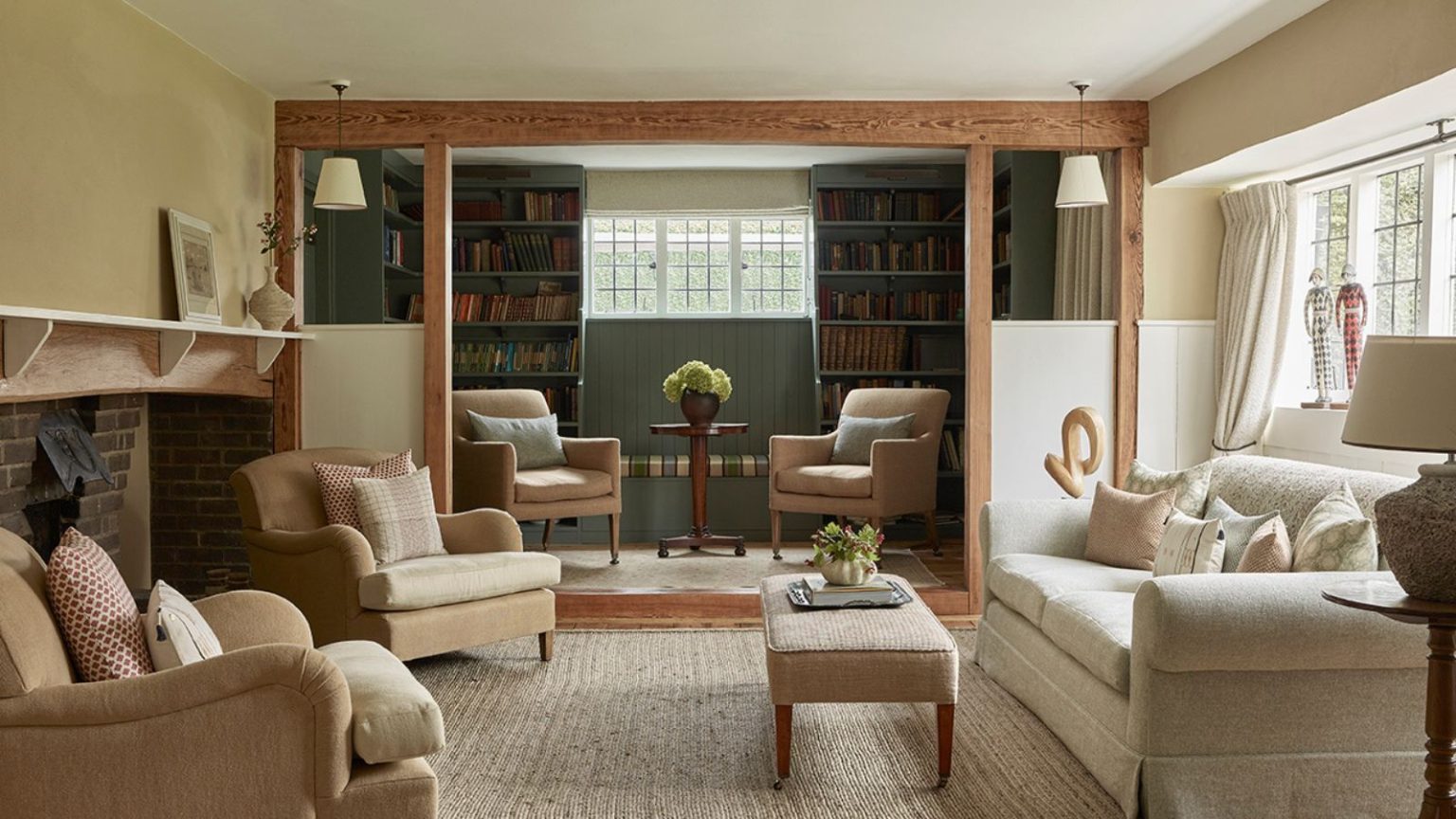 La couleur « calme » que tous les designers utilisent actuellement pour ajouter un calme instantané à n’importe quelle pièce Country cottage living room with cream sofa, beige armchairs, large brick fireplace, green painted library with bookshelves and two armchairs