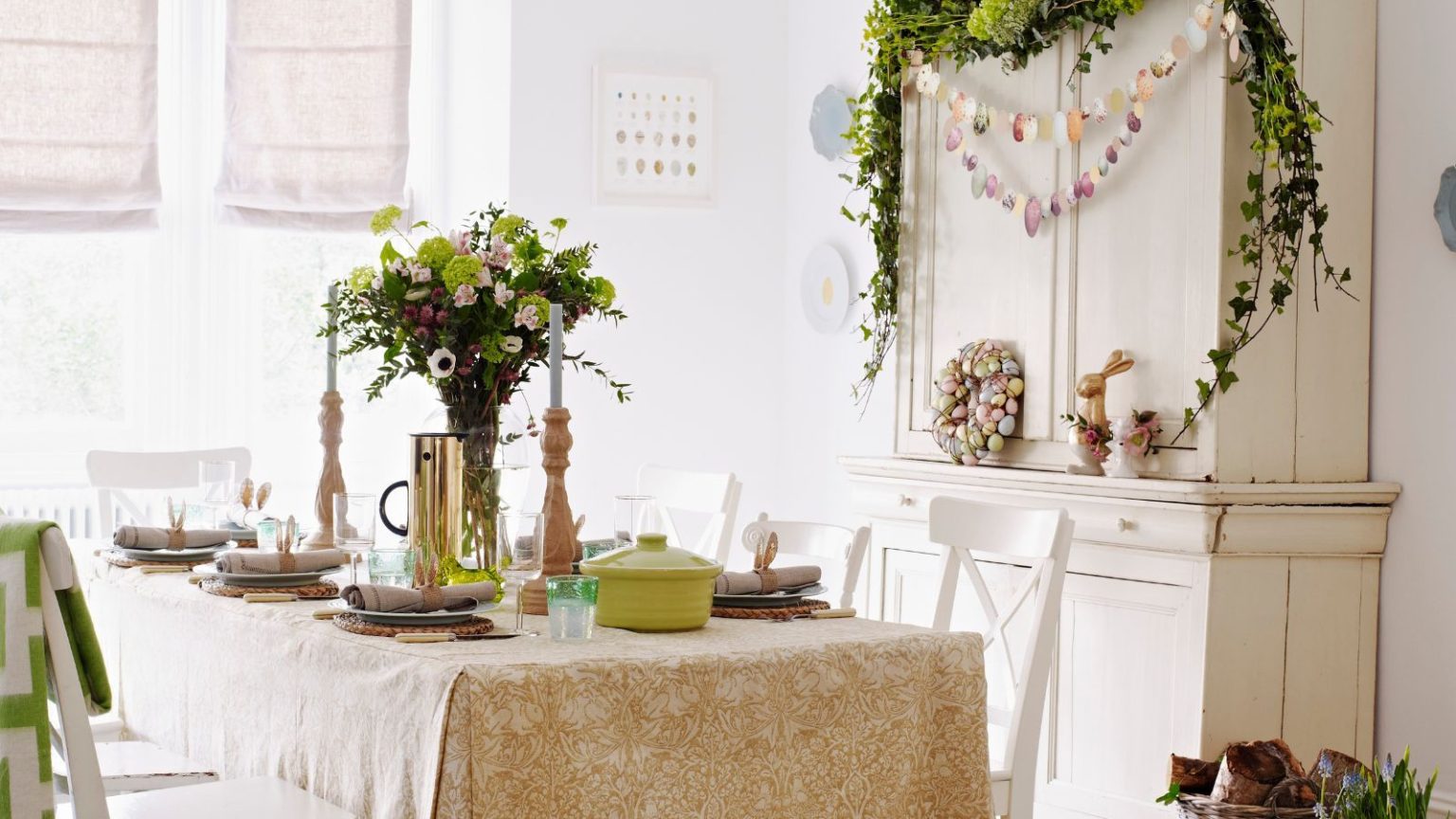 L’édition de Pâques : 20 décorations intemporelles que vous adorerez chaque printemps Table set for Easter with pale green and yellow theme, vase of flowers in the middle and a dresser next to the table with an Easter wreath and garland hanging on it