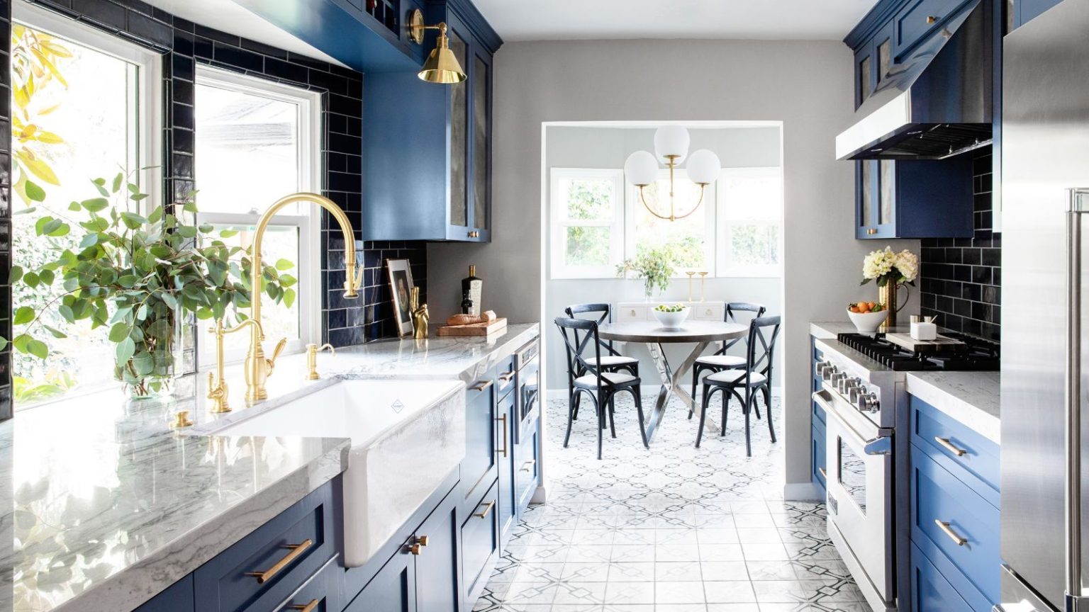 Les 5 teintes Farrow & Ball que les designers utilisent toujours pour égayer les petites cuisines A small kitchen leading into a dining room with dark blue cabinets, marble countertops, brass taps and fixtures.