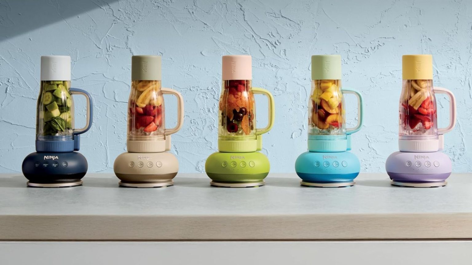 Je viens de mettre la main sur le nouveau mixeur Ninja Blendboss – c’est comme si les coupes Stanley et NutriBullet avaient un bébé A colourful set of five tumble style drinking cups, upside down on blender bases, against a blue wall