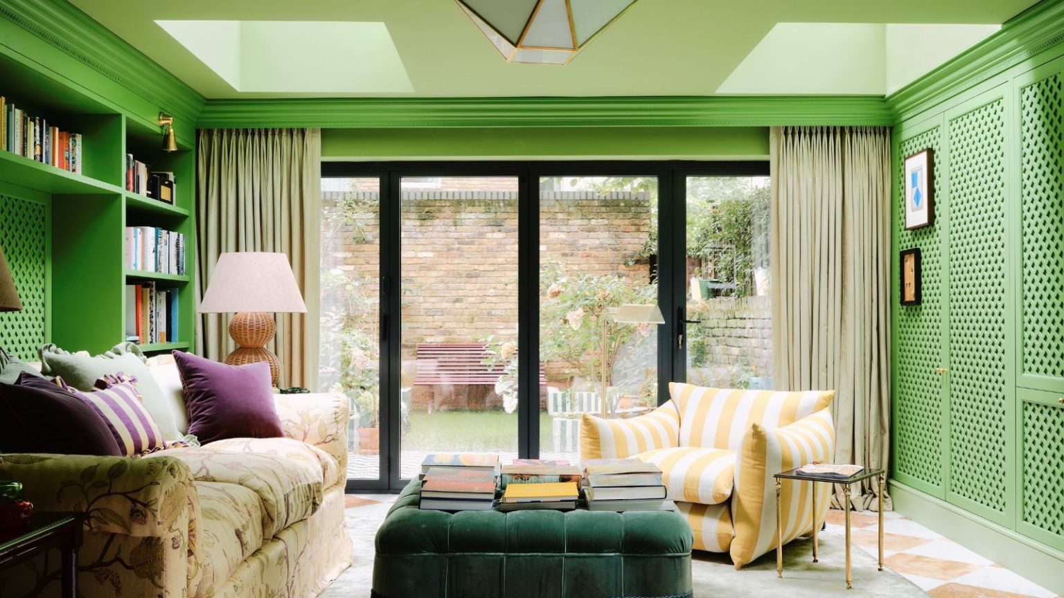 Fini les plafonds blancs – Le flou au plafond est une astuce de peinture géniale qui donne l’impression que les pièces sont instantanément plus grandes A media room with bright green walls, a light green ceiling with skylights, a wall of doors leading to a garden, and colorful decor.