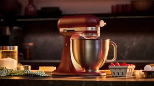 Le nouveau batteur sur socle Artisan Plus de KitchenAid transforme une cuisine de tous les jours en boulangerie professionnelle – c’est tout ce dont j’ai besoin pour réussir mon hébergement de printemps A red KitchenAid Artisan Plus Stand Mixer on a kitchen counter surrounded by baking ingredients.