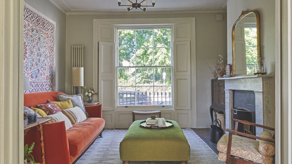 J’ai désespérément besoin de rangements chics mais travailleurs pour transformer mon petit salon – Ce sont les 9 solutions Wayfair abordables à mon problème Living room with bay window, marble fireplace, orange sofa, tapestry and green ottoman