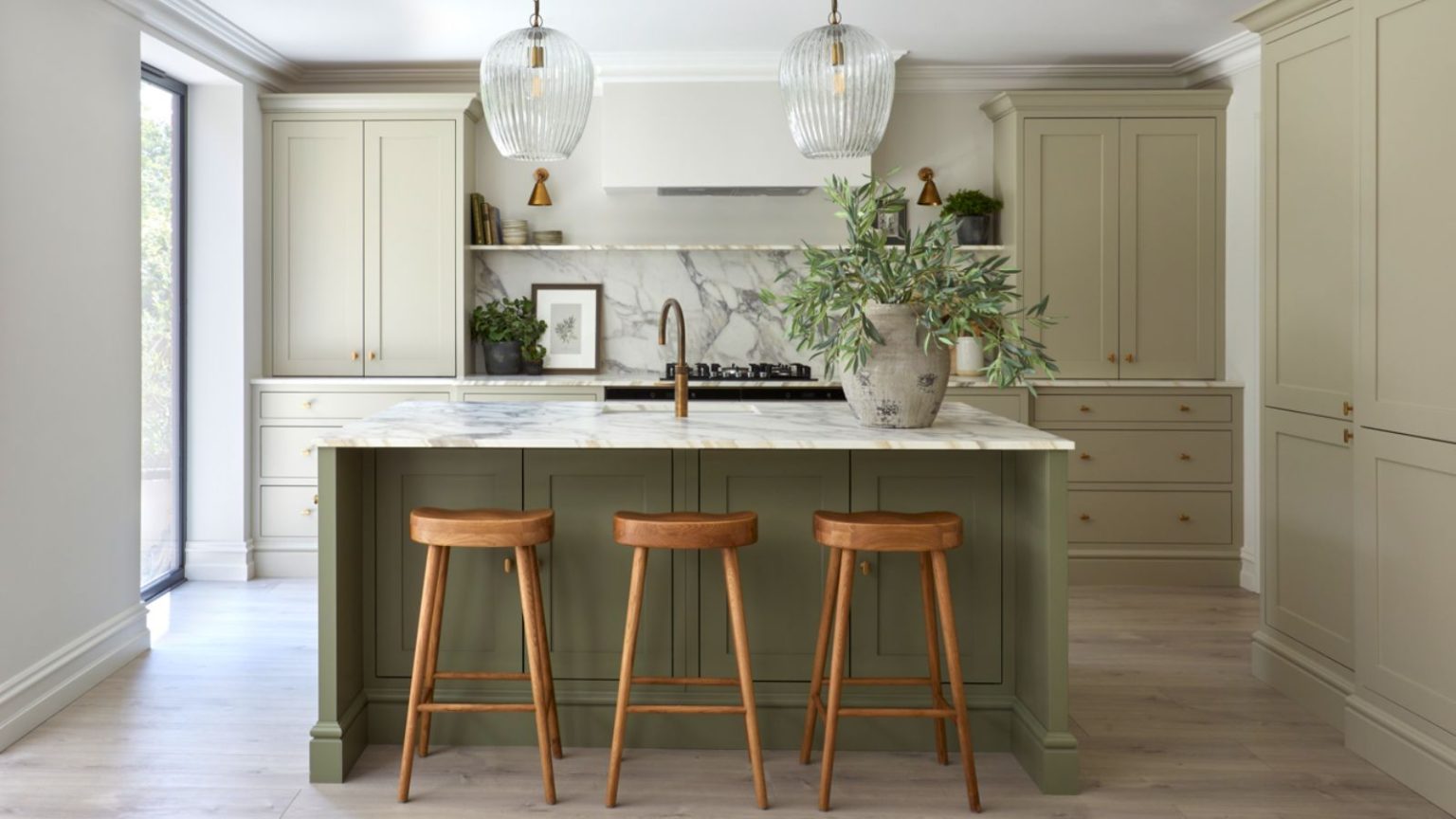 Cet incontournable d’épicerie ne devrait pas se trouver à proximité de votre cafetière haut de gamme – Voici pourquoi les experts disent que l’erreur peut être coûteuse (et quoi utiliser à la place) A kitchen with sage green cabinets and a darker green island. A large stone vase with green steps on the island beside a sink, and two glass pendants hanging from the ceiling above.