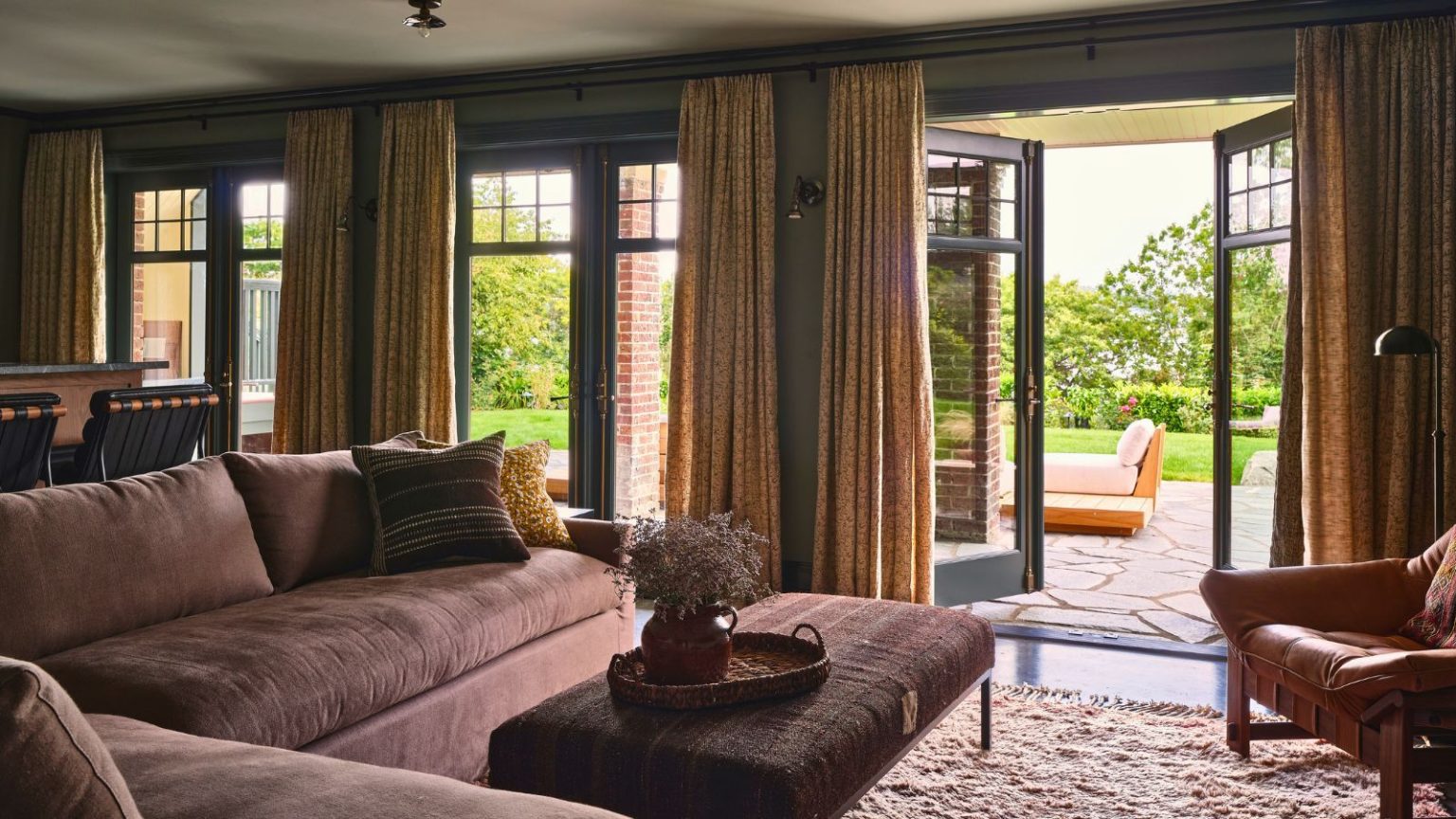 Cet accessoire d’aspirateur à 1 $ donne à toute votre maison une odeur de magasin d’anthropologie pendant que vous nettoyez Large living room area with L-shaped sofa, padded coffee table and rug. Double doors are open revealing bright outdoor area with outdoor seating, partially covered by yellow curtains.
