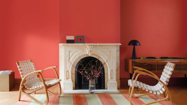 Benjamin Moore a dévoilé sa palette de couleurs printanières – c’est un équilibre non conventionnel de pastels sophistiqués et d’un rouge piquant et inattendu Living room with bright red walls, marble fireplace at the centre with a large modern painting propped up on it, two woven lounge chairs, a striped red and white rug, and a midcentury console in the corner with a black lamp on top of it.