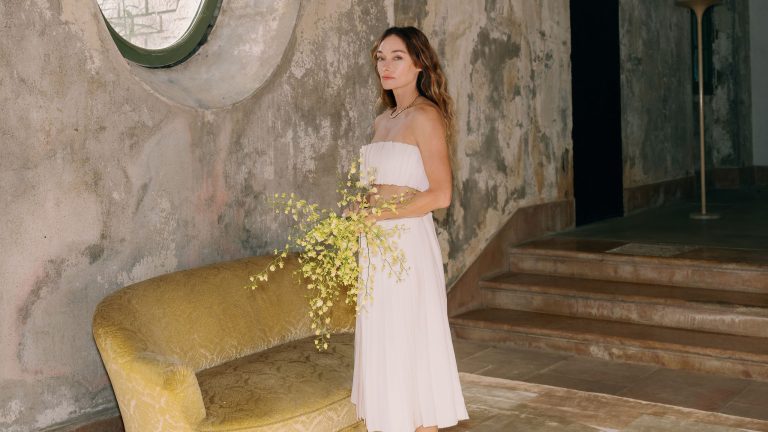 « Passer au crible les déchets, c’est amusant » – La créatrice superstar Kelly Wearstler explique comment elle parvient toujours à trouver les trésors dans la poubelle Kelly Wearstler stands in a brutalist room holding a bouquet of yellow flowers