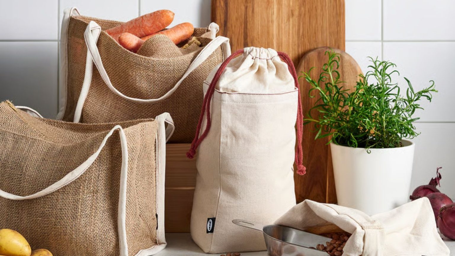 Les sacs de rangement en jute à 6 $ d’IKEA sont un moyen simple de réduire les déchets et de conserver les aliments frais cet été A set of cotton and jute food storage bags on a kitchen counter, beside some wooden cutting boards and a metal plant pot of herbs.