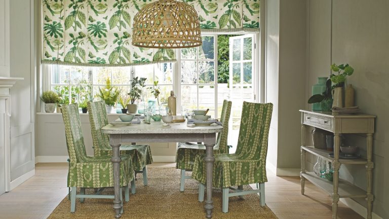 A green green dining room with a jute rug, light wood flooring, and a pale grey table, surrounded by four green and white patterned chairs.