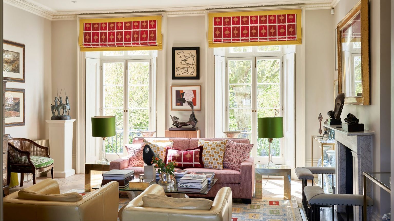 Vos fenêtres doivent être rafraîchies au printemps – 5 traitements approuvés par les concepteurs qui rehaussent instantanément votre espace Eclectic living room with large French doors leading out onto a balcony, pink and yellow blinds, pink sofa, coffee table with books and a vase, and two leather armchairs