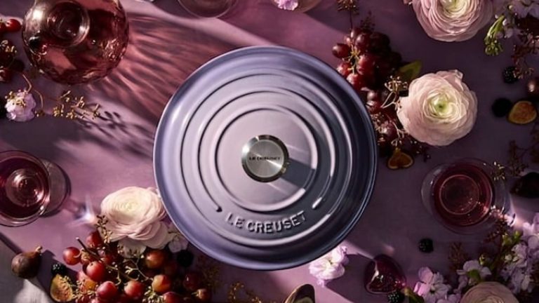 La plus jolie couleur printanière de Le Creuset est de retour après 6 ans de retraite – apportez une touche artistique de Provence à votre table avant qu’elle ne soit épuisée A purple lid to a Le Creuset Dutch oven viewed from above, on a purple worktop, surrounded by purple and light pink flowers