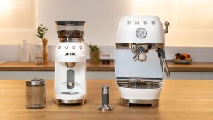 Enfin une cafetière chic qui trouvera sa place dans ma petite cuisine – le dernier tout-en-un de SMEG apporte le style rétro aux espaces exigus A cream retro manual coffee mahcine beside a matching coffee grinder on a wooden kitchen counter