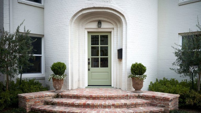 A warm white home exterior with a soft green front door in an arched doorway.