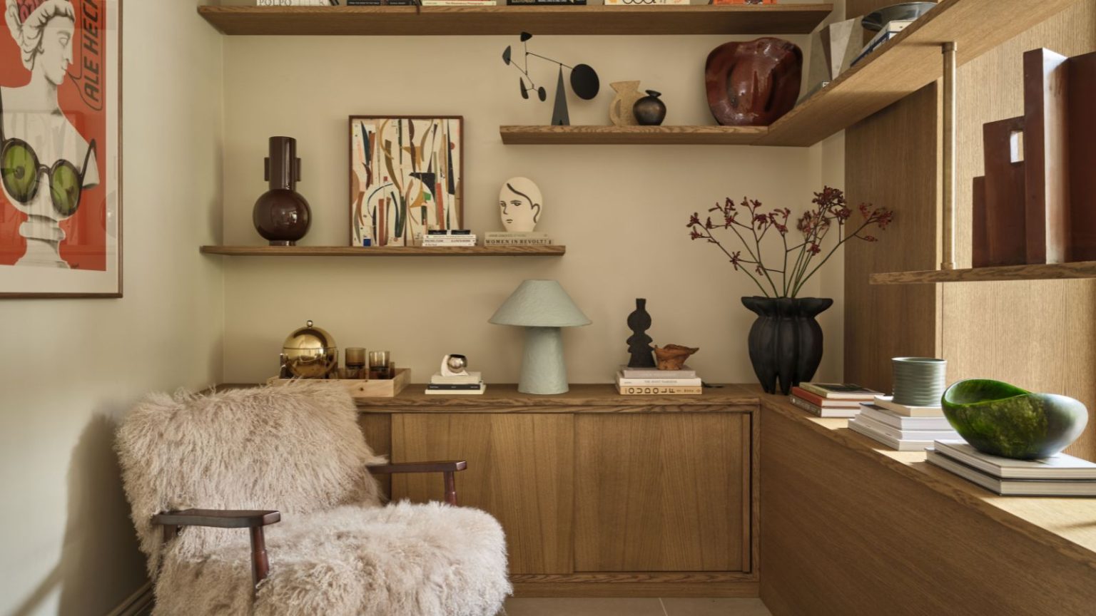 Quel stockage rend une maison chère en 2026 ? Les designers disent que ce sont ces 5 styles de luxe Reading corner with wooden shelves decorated with vases and artwork, a fluffy armchair, and a large red print on the wall