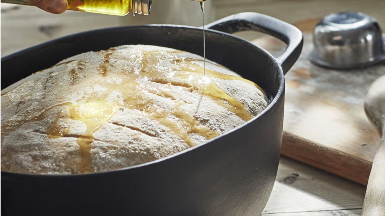 J’ai comparé le IKEA Dutch à 60 $ au Heritage Le Creuset – et j’ai été sérieusement surpris par le résultat A black cast iron oval pot with a risen bread dough inside, someone pouring oil on top