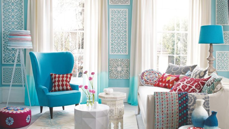 Cette astuce victorienne oubliée donne à votre maison une odeur incroyable – et elle ne nécessite que 2 ingrédients Bright and colorful patterned living room with blue walls, a blue chair, white couch, blue lamp, white coffee table with flowers, and patterned blankets, cushions, pouffe, table, lamp shade and vases.
