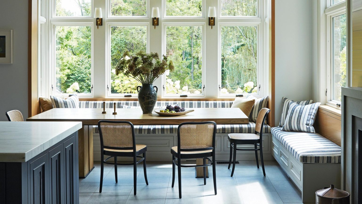 Ils sont tombés amoureux de sa « vieille âme » – cette maison du New Jersey est désormais une classe de maître en élégance sobre et moderne a light and bright kitchen dining area with a striped large banquette, ceiling beams and blue tiled floor