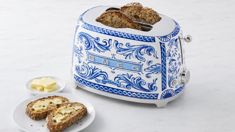 A blue and white patterned SMEG toaster on a white marble counter beside a plate of buttered toast