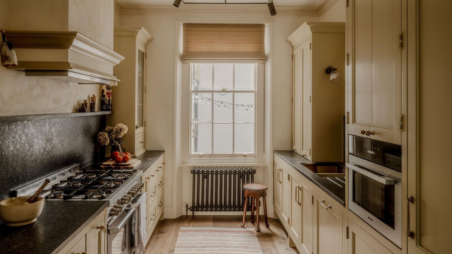 Cette maison de ville de Londres prouve qu’adopter les bizarreries « farfelues » est le secret d’une maison pleine de caractère a warm butter yellow kitchen in a London townhouse with georgian window and dark countertops