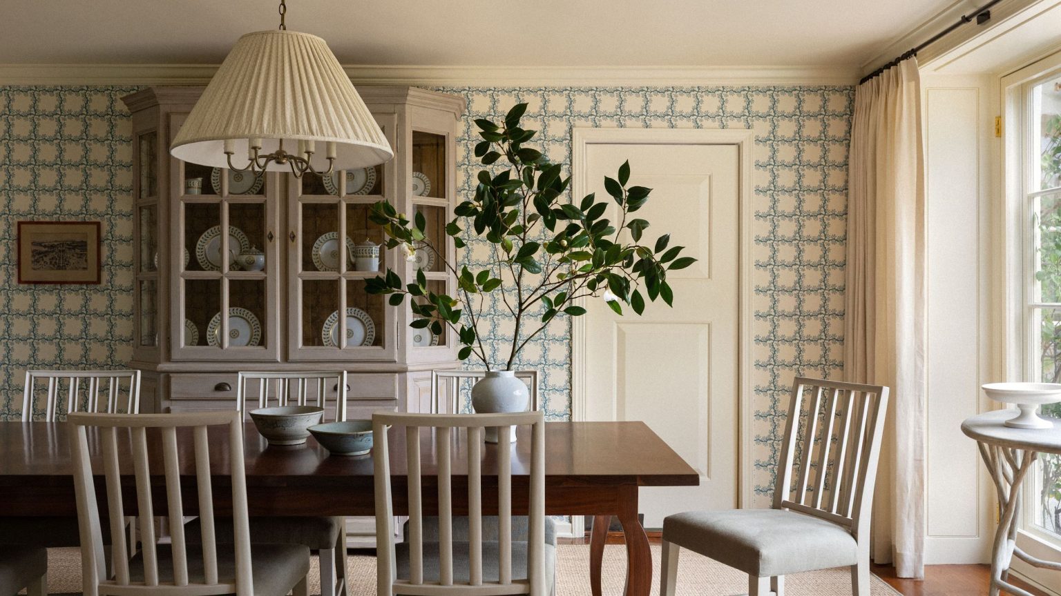 24 pièces pour apporter l’esthétique du jardin de campagne anglais à l’intérieur – et la laisser se répandre à nouveau Sun-drenched dining room featuring blue-and-white rose-motif wallpaper, airy white dining chairs, a pleated pendant light, and a large potted plant