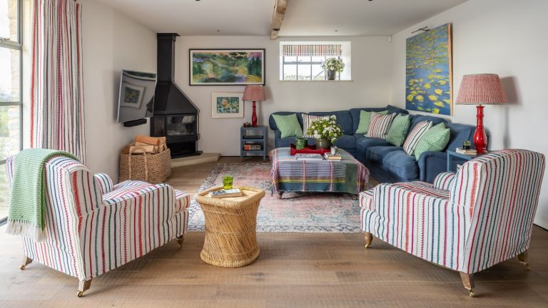 Les experts en CVC affirment que cette règle simple de placement du purificateur d’air améliorera considérablement les performances pour de bon A bright and colorful living room with striped chairs, a patterned rug, blue corner sofa, rattan side table, black wood burner, and red lamps. The walls are white, with a large window to the left.