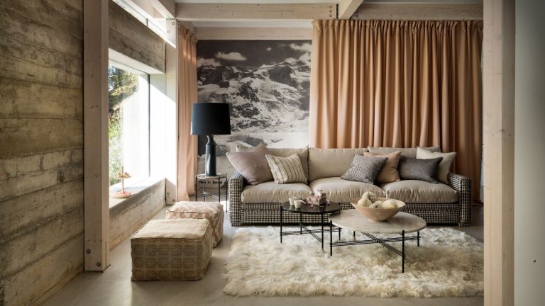 Vous en avez assez de voir vos tapis glisser sur le sol ? Je jure par ce correctif à 8 $ pour Zero Budge A modern statement living room with exposed wood panelling, a white fluffy rug, a brown sofa, statement wallpaper and peach colored curtain.