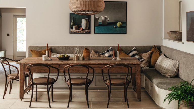 a large banquette dining nook in an English country home with upholstered storage bench seat, rustic wooden table and vintage chairs