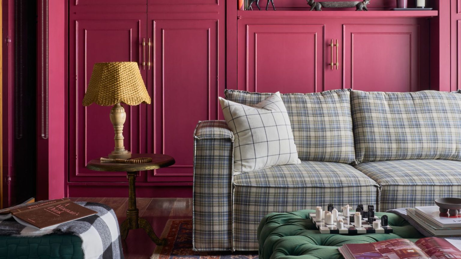 Le rose framboise pourrait être la couleur inattendue de l’été – les créateurs disent qu’il est joyeux, luxueux et qu’il « fait tout le travail pour vous » Living room with raspberry pink cabinetry, plaid blue sectional sofa, Persian rug, green velvet ottoman, side table with lamp and plant on the floor