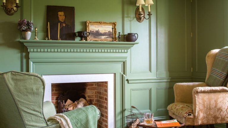 Living room with fireplace and walls painted in Calke Green by Farrow &amp; Ball, two armchairs, and a mantelpiece with antique paintings, vases and candlesticks
