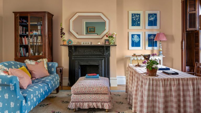 Ces bureaux à domicile « pour lui et pour elle » dans un Brownstone de New York prouvent que des projets audacieux peuvent stimuler la concentration – sans en détourner l’attention a pink womens home office with an original black fireplace, pink gingham skirted desk, floral ottoman and blue floral sofa