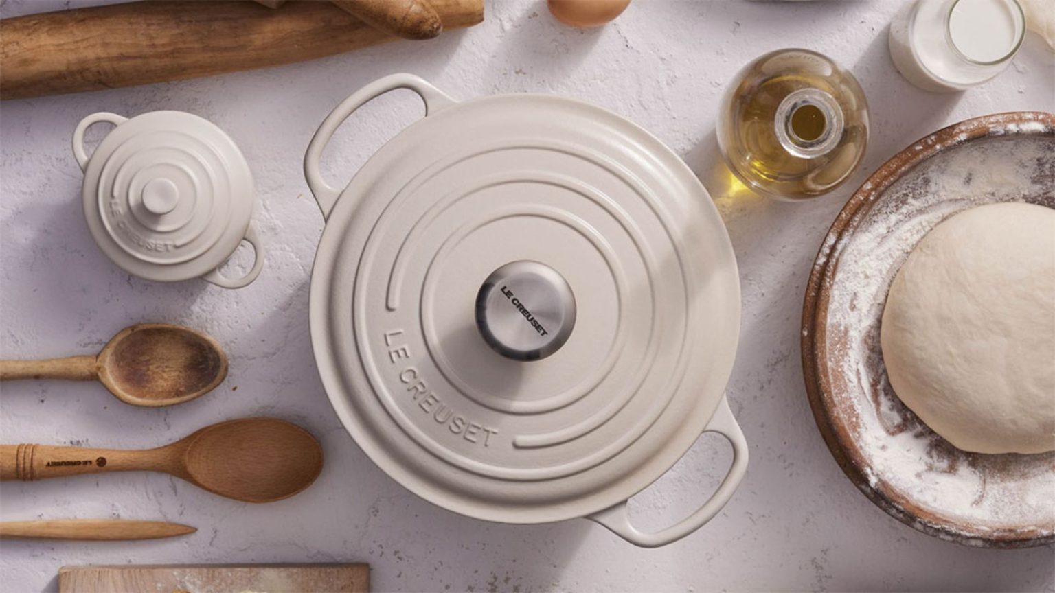 Il s’agit du plat de service Le Creuset que les créateurs utilisent pour passer directement du four à la table de la fête des mères, vous permettant ainsi d’économiser de l’espace de stockage convoité. A cream colored Le Creuset Dutch oven viewed from above, with a small cocotte version beside it. With wooden baking utensils, and a bowl of bread dough beside it.